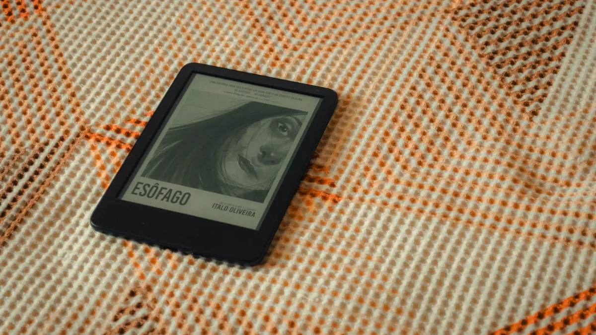 An ereader resting face-up on a textured blanket, its screen showing a book cover.