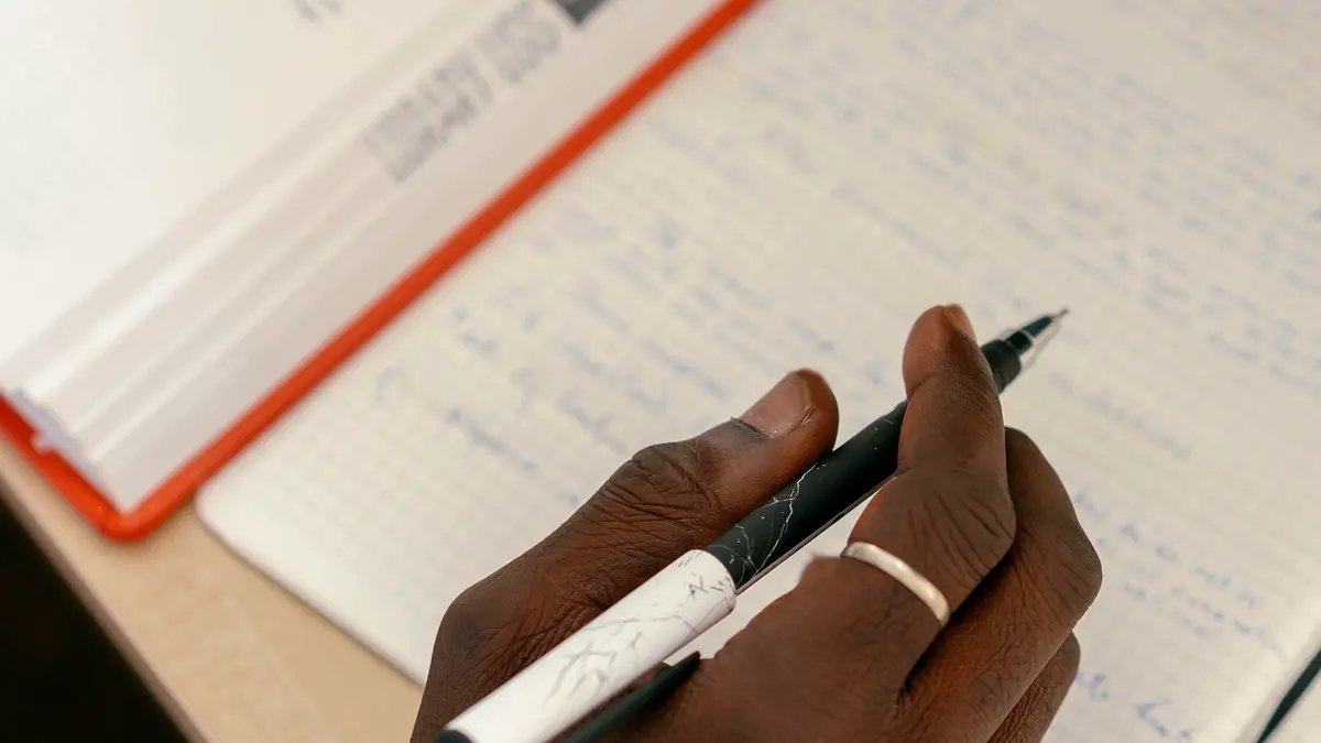A hand writing in a notebook beside an open book.