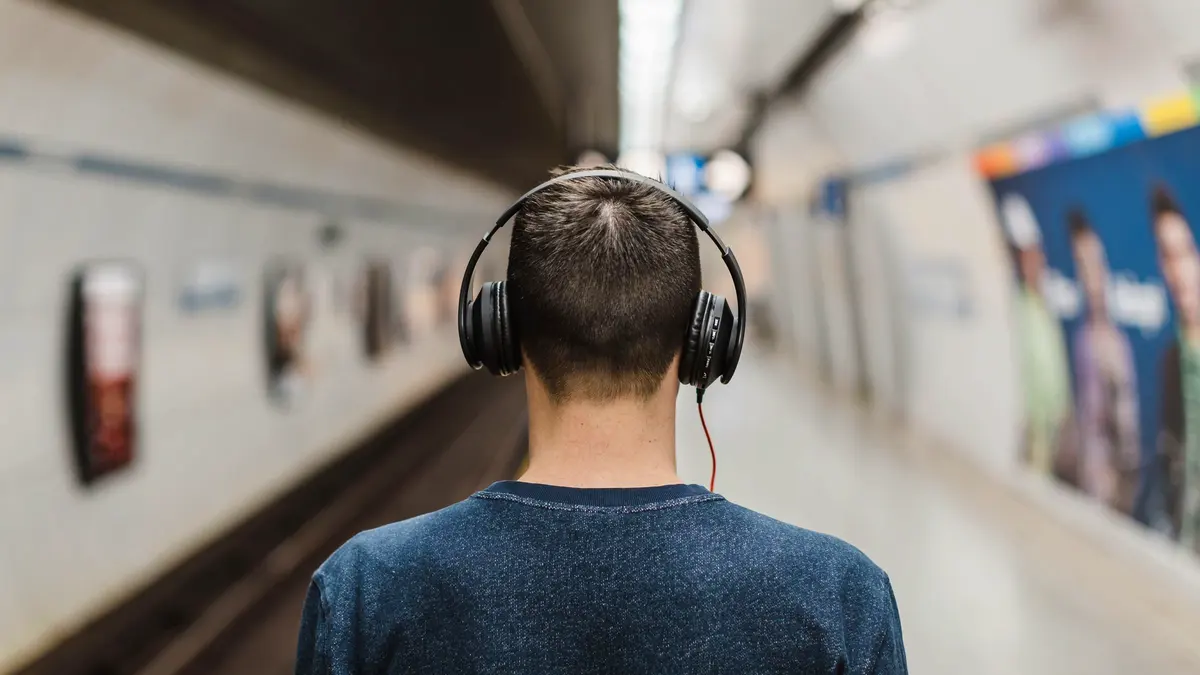 Someone wearing headphones beside a railway platform.