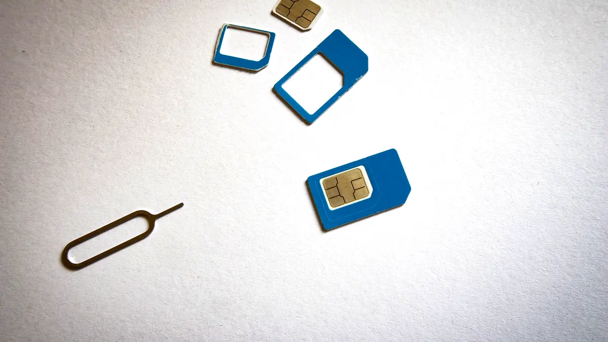 SIM cards beside a SIM ejector tool on a white surface.