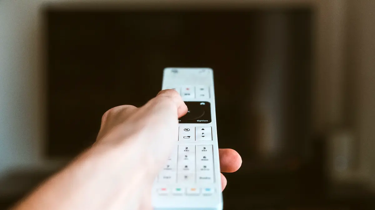 A hand holding a remote control in front of a television.