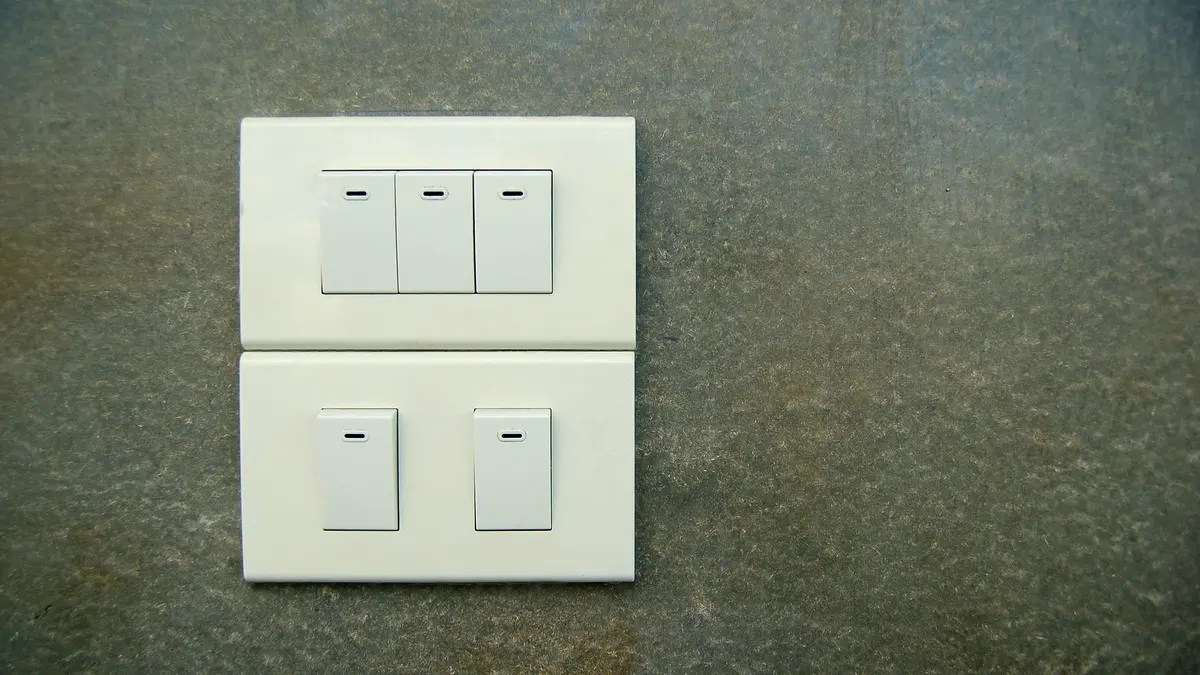 Two white rocker light switch plates on a grey wall.