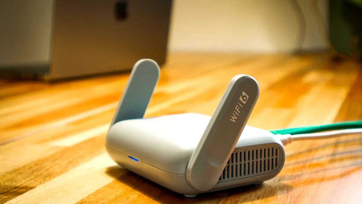 A Wi-Fi router on a wooden desk with an Ethernet cable plugged into the back.
