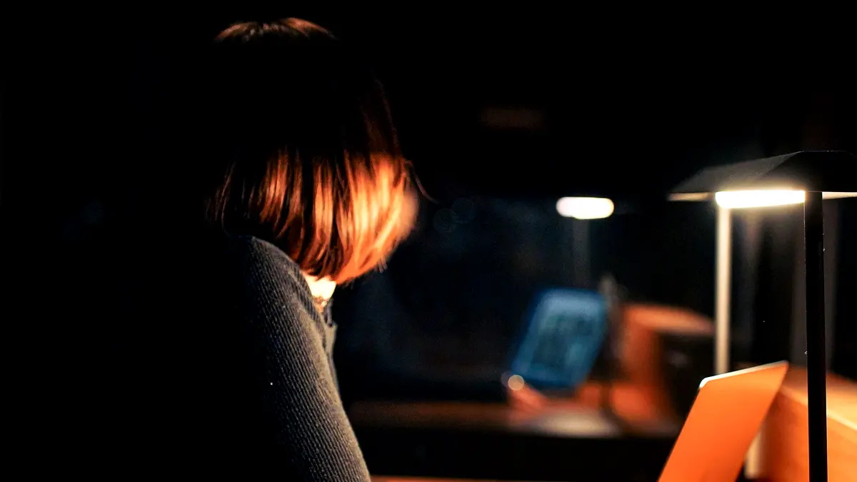 A person working at a desk lit only by a lamp, the rest of the office dark.
